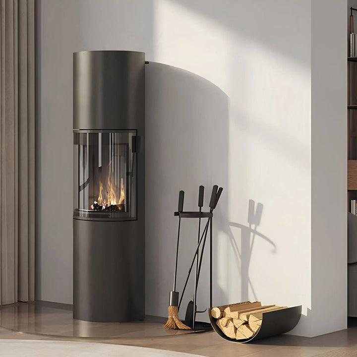 Kaminofen CERA DESIGN Prego XL | 6 kW – Runder grauer Kaminofen neben Kaminbesteck und Holzablage im Wohnraum