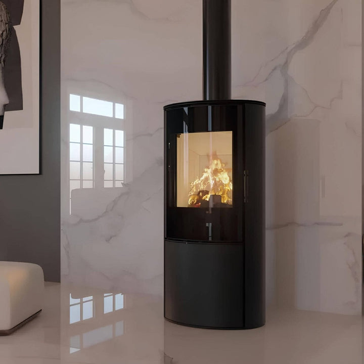 Kaminofen Hitze Ellisse S 5,3 kW – Kaminofen mit Feuer und Rauchrohr vor einer hellen Steinwand