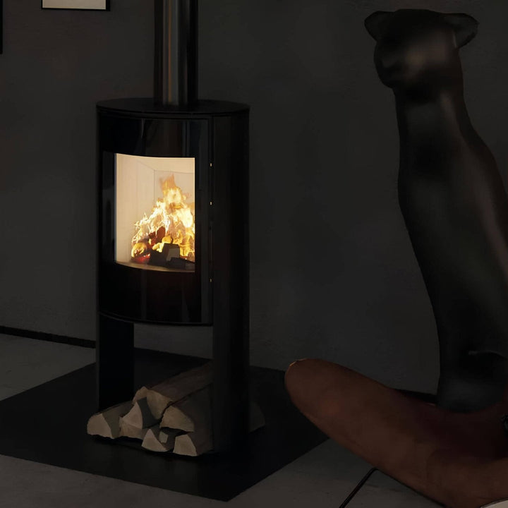 Kaminofen Hitze Ellisse SB 5,3 kW – Kaminofen mit Feuer und Holzfach neben einem Ledersessel