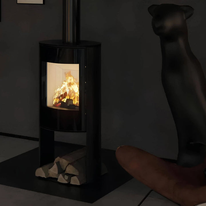 Kaminofen Hitze Ellisse SB – Kaminofen mit Feuer und Holzfach neben einem Ledersessel