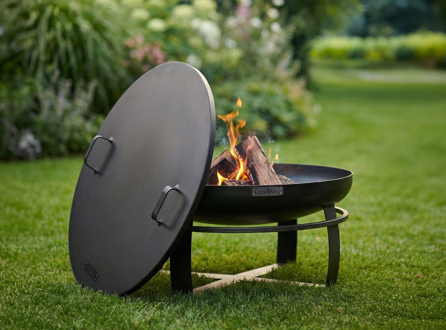 CookKing Viking Feuerschale 80 cm mit brennendem Holzfeuer und Deckel auf einer grünen Rasenfläche im Garten