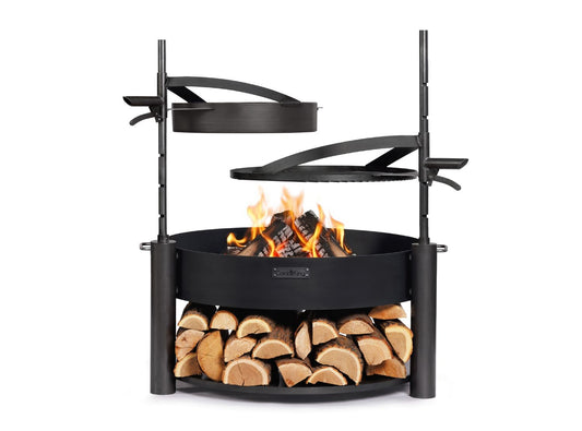 Feuerschale MONTANA X 80 cm mit brennendem Holz, höhenverstellbarem Grillrost und Stahlpfanne sowie Holzlagerung im unteren Bereich