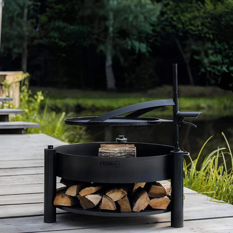 Multifunktionale Feuerschale MONTANA X + Grillrost – Feuerschale mit schwenkbarem Grillrost und Holzablage auf einer Terrasse
