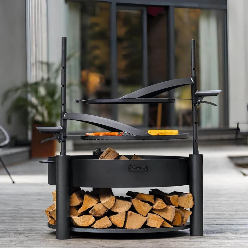 Multifunktionale Feuerschale MONTANA X + Grillrost – Feuerschale mit zwei Grillaufsätzen und gefüllter Holzablage auf einer Terrasse