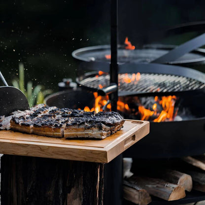 Multifunktionale Feuerschale MONTANA X + Grillrost – Nahansicht von Grillgut auf einem Holzbrett vor der Feuerschale