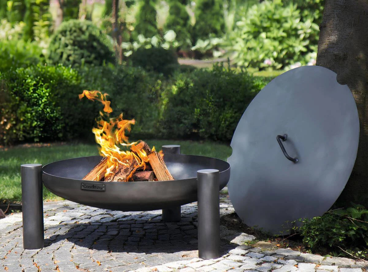 CookKing Feuerschale Palma mit Flammen im Garten; der runde Deckel lehnt daneben