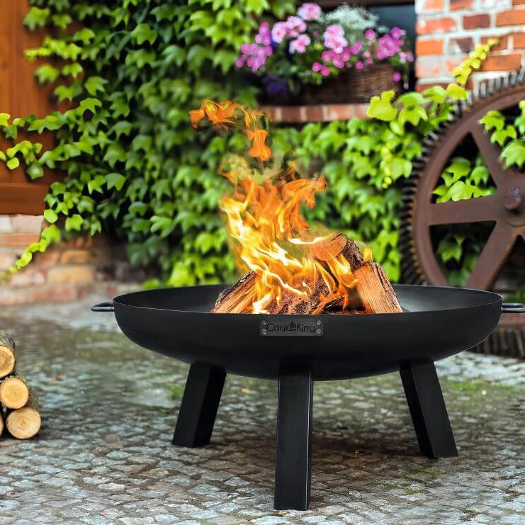 CookKing Feuerschale Polo mit brennenden Holzscheiten vor einem Blumenbeet