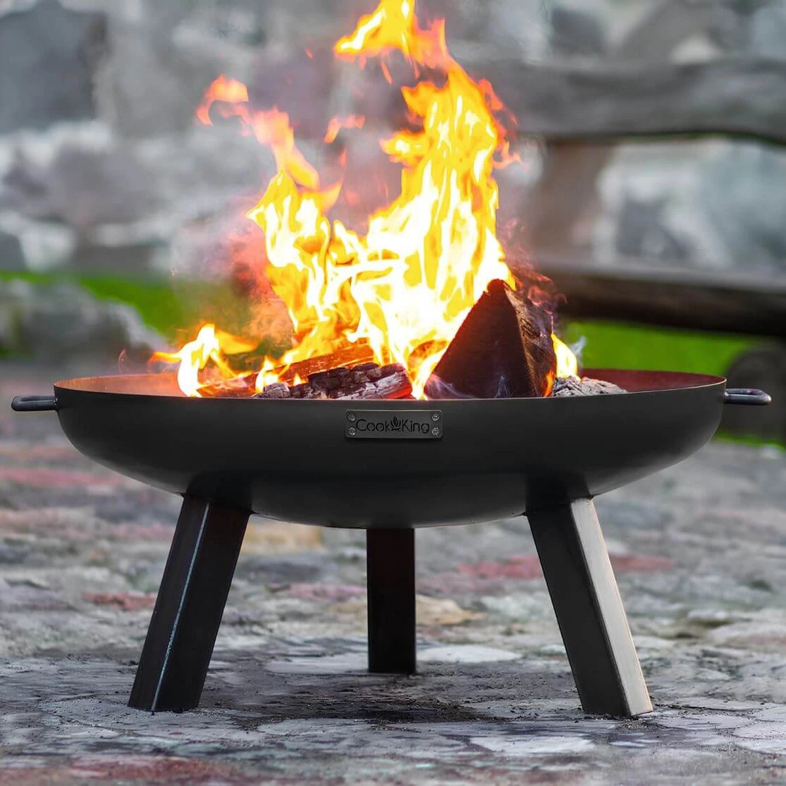 CookKing Feuerschale Polo mit hoher Flamme auf Pflaster vor einer Steinmauer