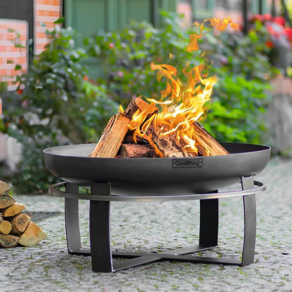 Feuerschale CookKing Viking – Feuerschale mit Feuer neben Holzscheiten im Garten