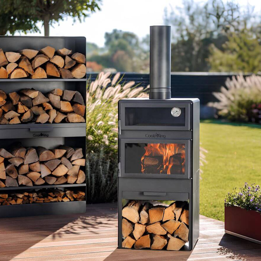 CookKing Gartenofen Vento mit Backfach – Gartenofen mit Backfach und Feuer neben einem Kaminholzregal im Garten