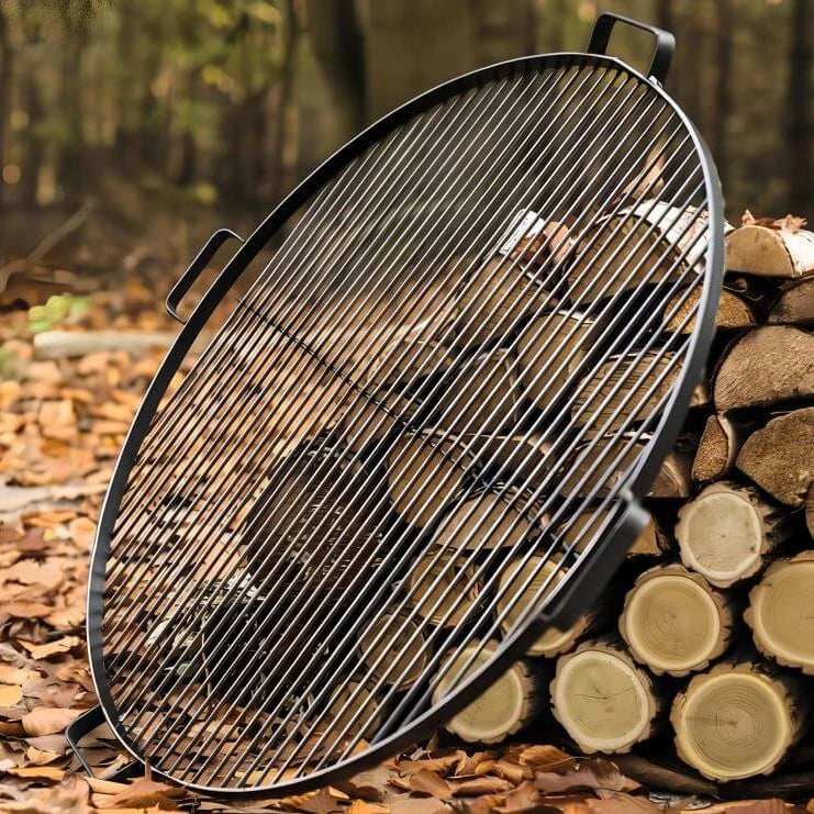 Runder CookKing Grillrost aus Naturstahl mit vier Griffen an gestapelten Holzscheiten