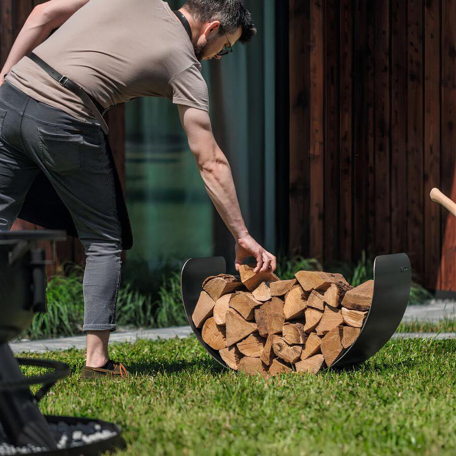 CookKing Kaminholzregal Turyn – Befüllen des halbrunden Kaminholzregals mit Holzscheiten im Garten