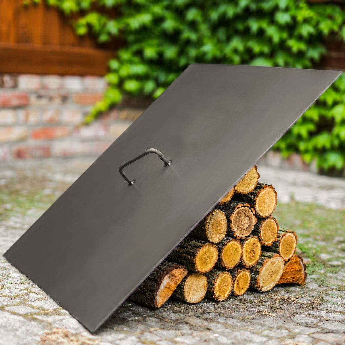 Deckel für Feuerschalen – quadratisch – Quadratischer Deckel mit Griff an einem Holzstapel im Garten