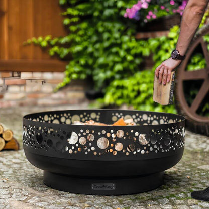 Feuerschale CookKing Boston 80 cm – Einlegen eines Holzscheits in die Feuerschale im Garten