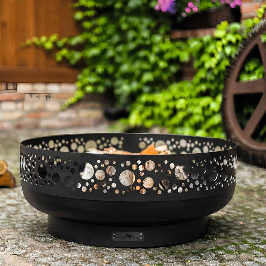 Feuerschale CookKing Boston 80 cm – Feuerschale mit Lochmuster und Holzscheiten auf Gartenpflaster