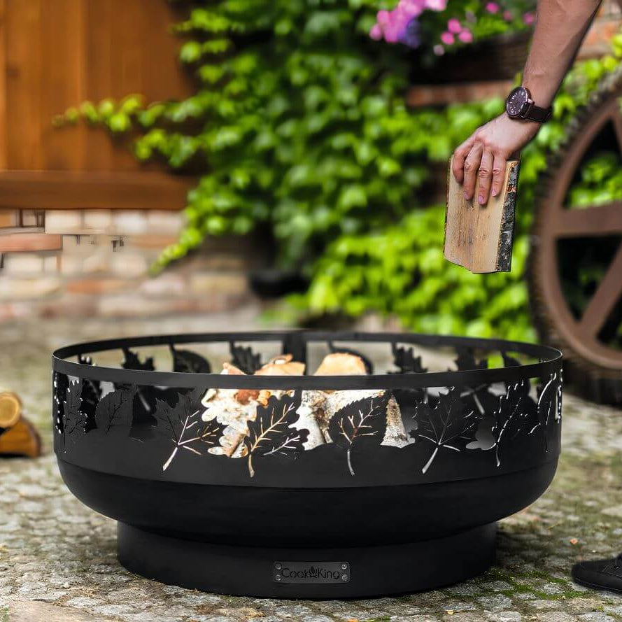Feuerschale CookKing Toronto 80 cm – Einlegen eines Holzscheits in die Feuerschale im Garten