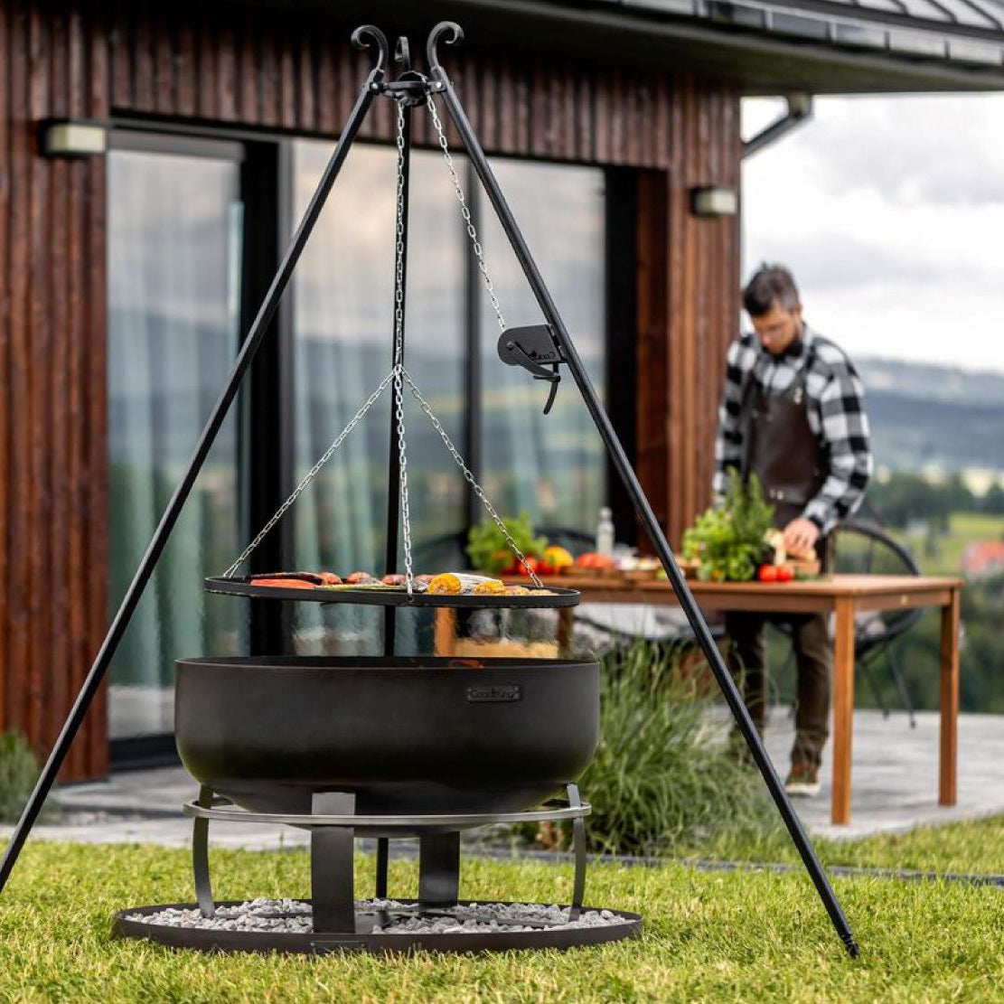 Feuerschale Viking XXL 80 cm + Schwenkgrill 180 cm mit Kurbel + Grillrost  70 cm und Feuerschalenbasis rund – Feuerschale und Schwenkgrill neben einer Gartenhütte