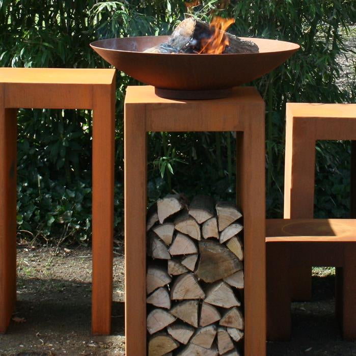 FORNO HALO Feuerschale aus Stahl mit brennendem Holz auf einem Holzlagertisch – Anwendungsansicht