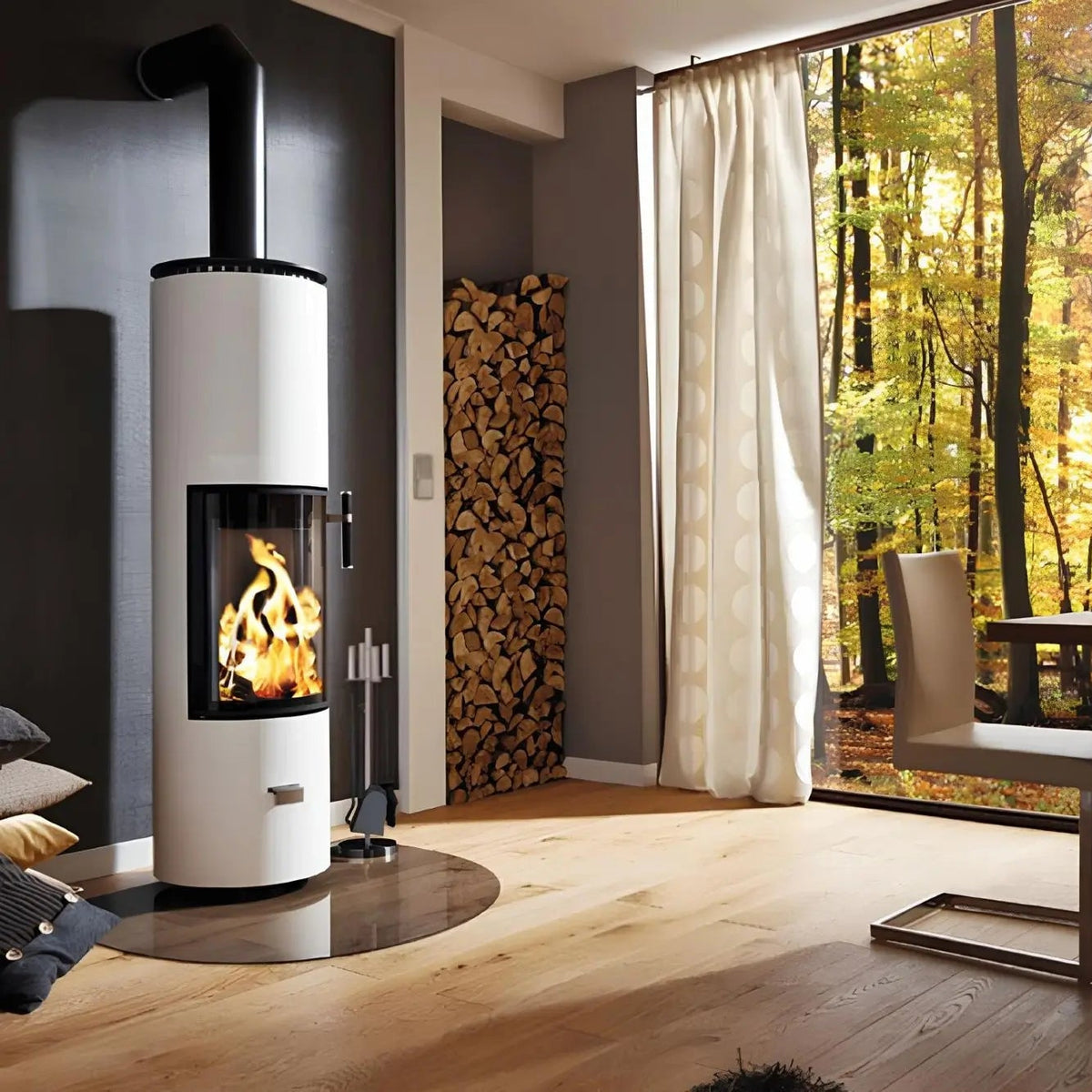Kaminofen CERA DESIGN Solitherm | 6 kW – Runder heller Kaminofen neben einem großen Fenster mit Waldblick