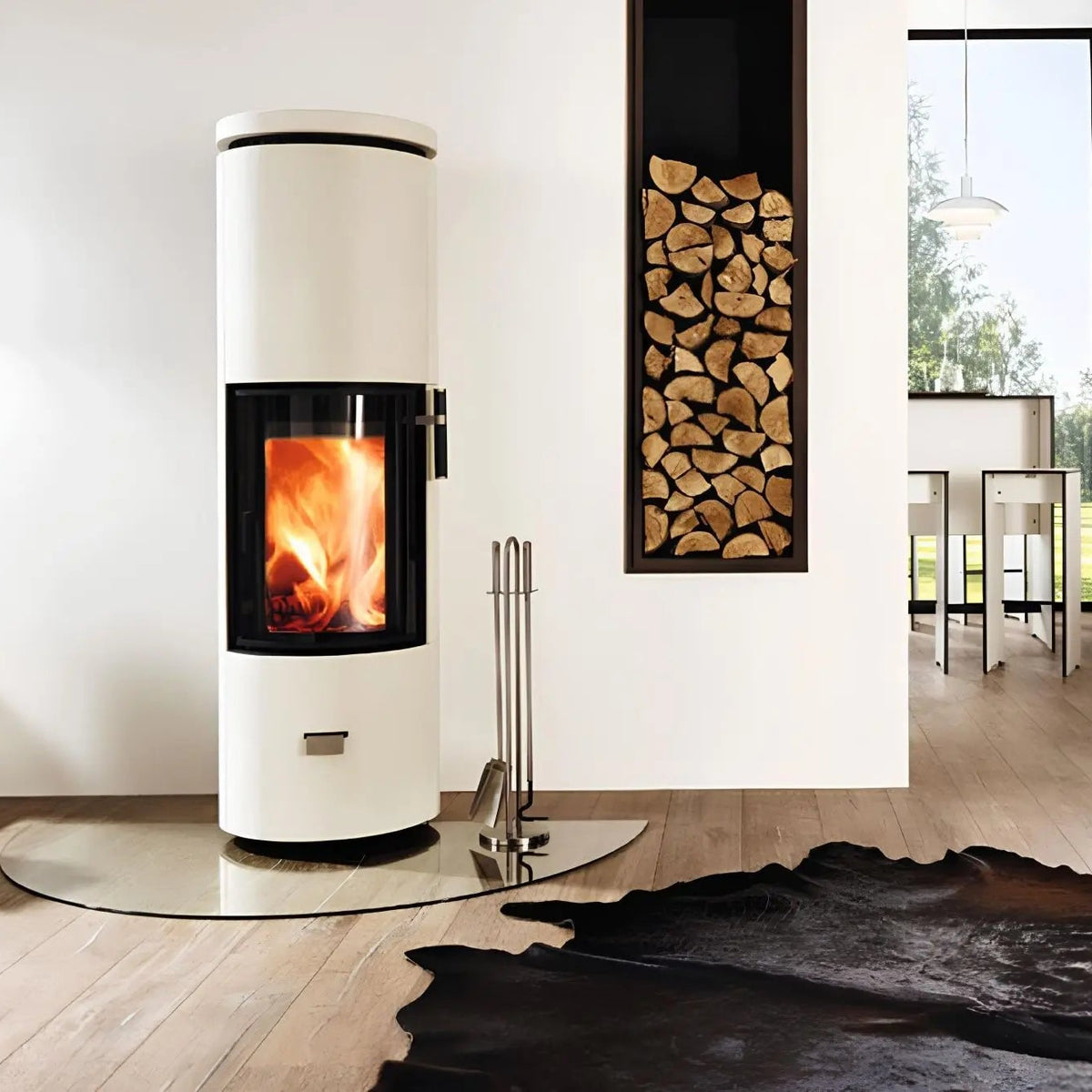 Kaminofen CERA DESIGN Solitherm Beton | 6 kW – Runder heller Kaminofen auf einer Glasplatte neben einer Holznische