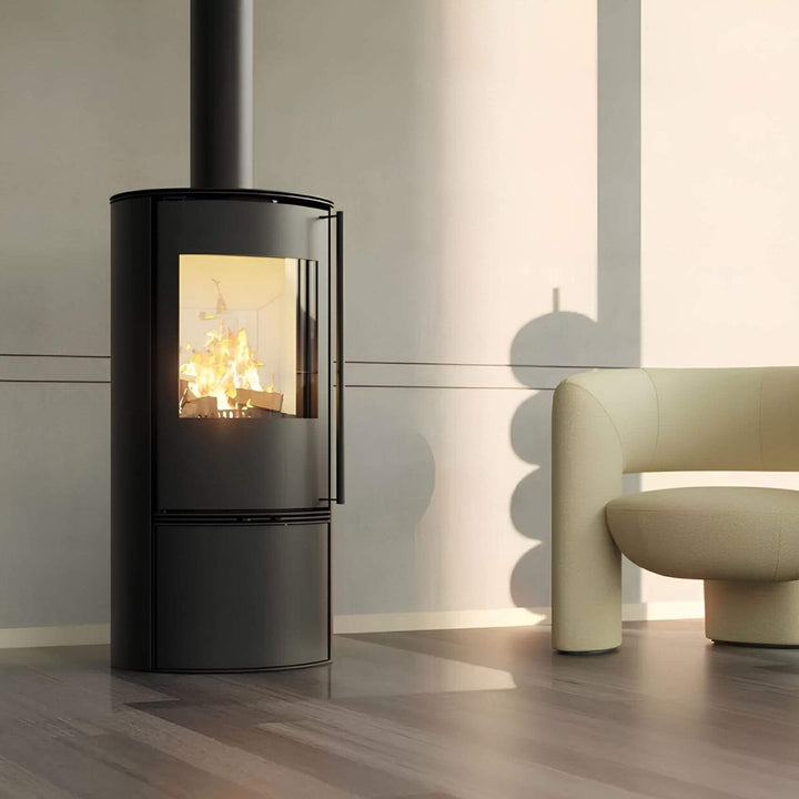 Kaminofen Hitze Bane 5 kW – Kaminofen mit Feuer neben einem hellen Sessel