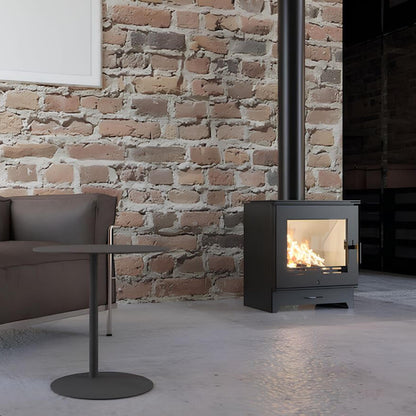 Kaminofen Hitze Gatto ME 5,3 kW – Kaminofen mit Feuer neben Ledersessel und Ziegelwand