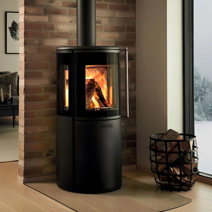 Kaminofen Varde Ovne Nordic 9 Air 6,2 kW – Kaminofen mit Feuer vor einer Ziegelwand und Holzkorb