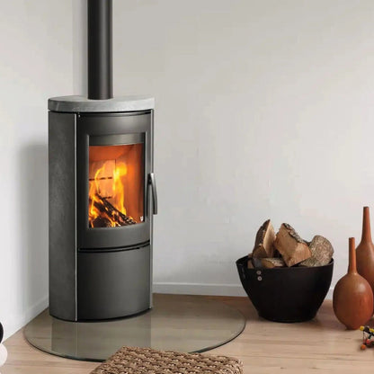 Kaminofen Varde Ovne Shape 2 Air Speckstein 5 kW – Kaminofen mit Specksteinverkleidung, Feuer und Rauchrohr neben einem Holzkorb