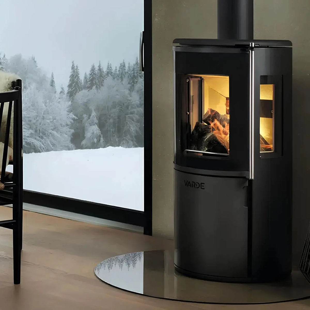 Kaminofen Varde Ovne Nordic 7 Air 6,2 kW – Kaminofen mit Feuer neben einem Fenster mit Schneelandschaft