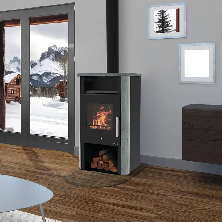 Kaminofen Wamsler Cube Naturstein | 6 kW – Kaminofen mit Natursteinseiten und Rauchrohr neben Fenstern mit Bergblick