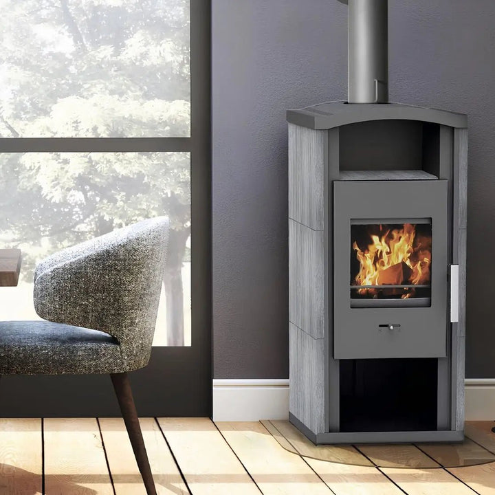 Kaminofen Wamsler Gron | 6 kW – Kaminofen mit Feuer und Rauchrohr neben einem Sessel