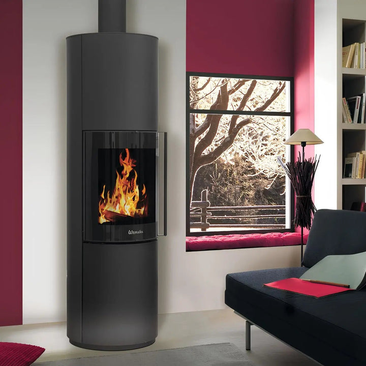 Kaminofen Wamsler Rook | 6,3 kW – Hoher runder Kaminofen mit Rauchrohr neben einem Fenster im Wohnraum
