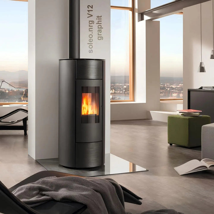 Pelletofen Wodtke soleo.nrg V12 air+ | 6/8 kW – Runder graphitfarbener Pelletofen auf einer Glasplatte im Wohnraum