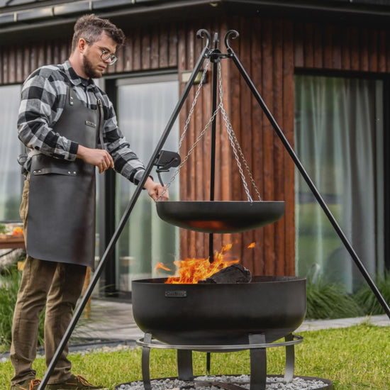 Video: Outdoor-Grillstation mit Schwenkgrill, Viking XXL Feuerschale und runder Steinbasis auf einer Rasenfläche vor modernem Holzhaus.