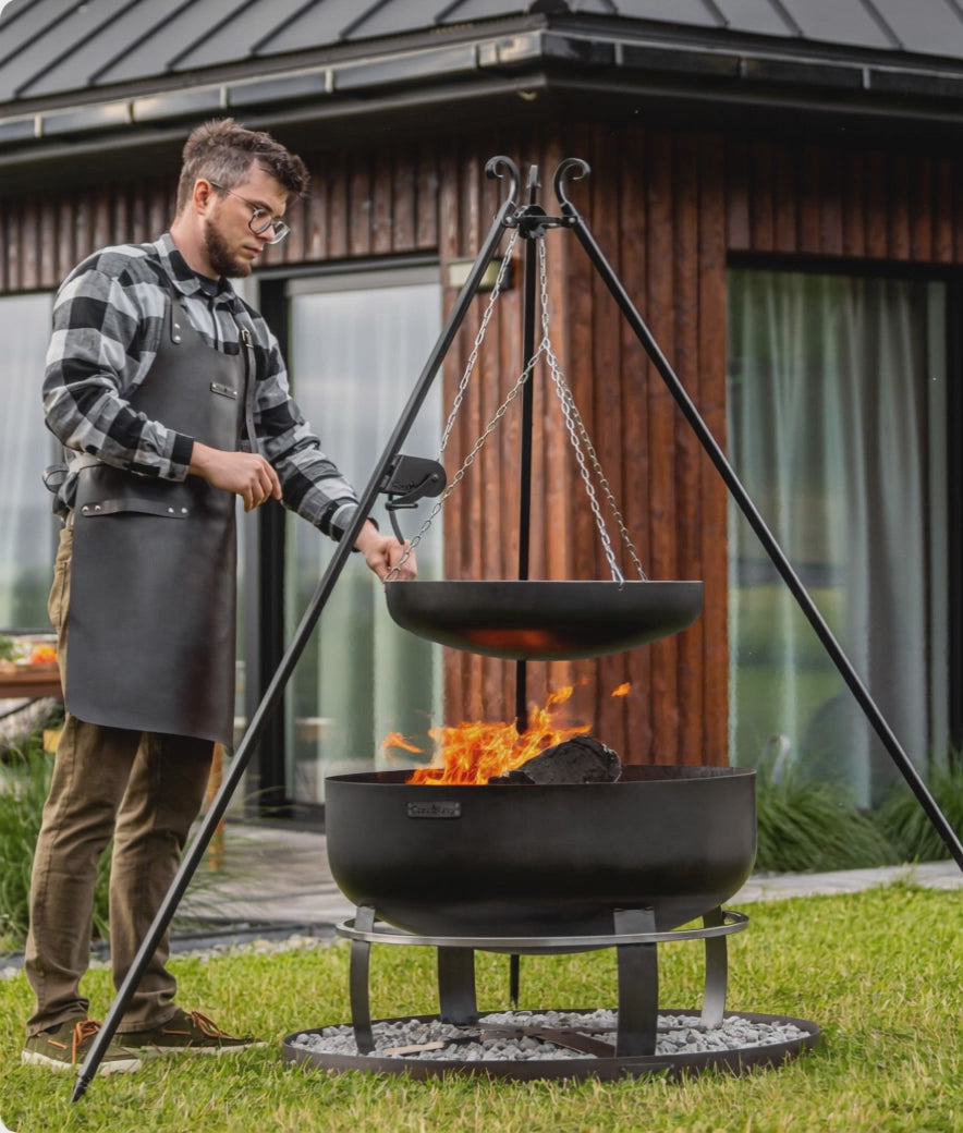 Video: Outdoor-Grillstation mit Schwenkgrill, Viking XXL Feuerschale und runder Steinbasis auf einer Rasenfläche vor modernem Holzhaus.
